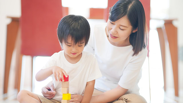 障害者の子供と大人の女性が室内で積み木遊びをしている様子。笑顔で交流している。.
